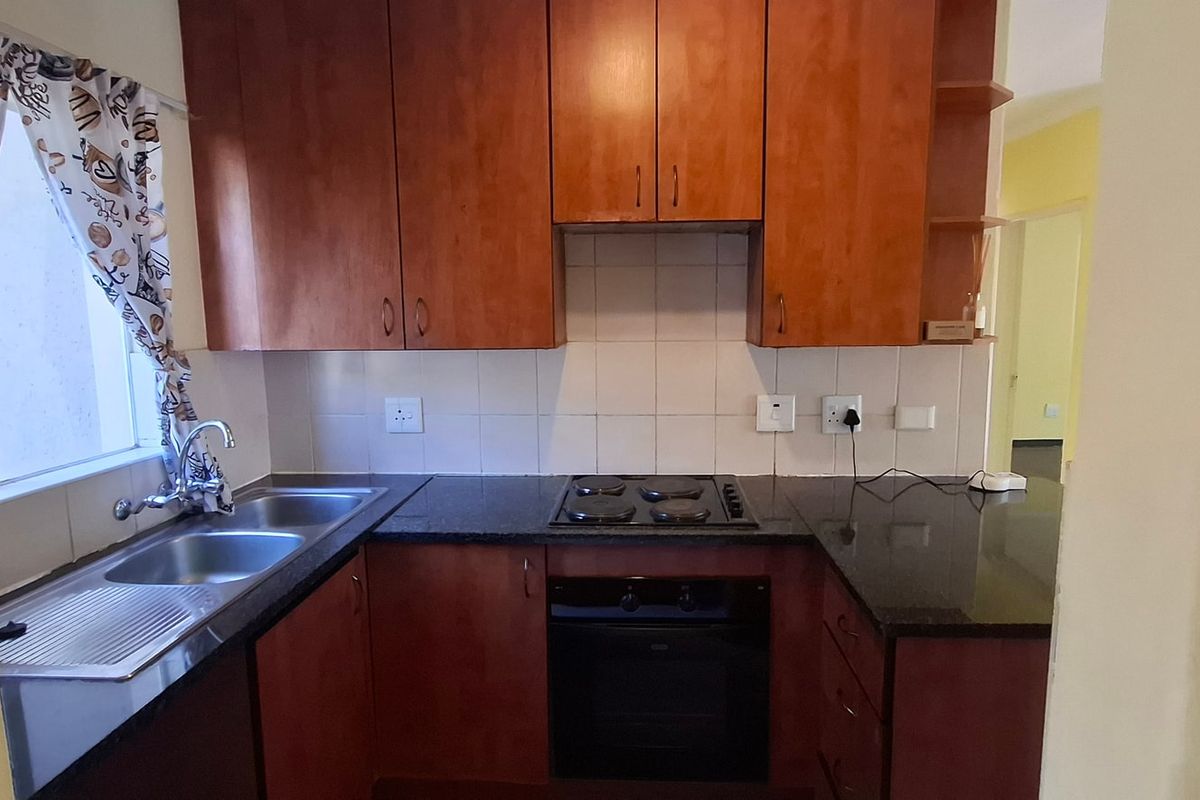 A functional kitchen featuring warm-toned wooden cabinetry, granite countertops, a double stainless steel sink, and a built-in electric oven with a hob.