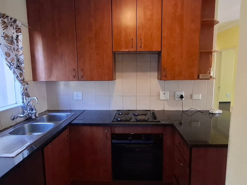 A functional kitchen featuring warm-toned wooden cabinetry, granite countertops, a double stainless steel sink, and a built-in electric oven with a hob.