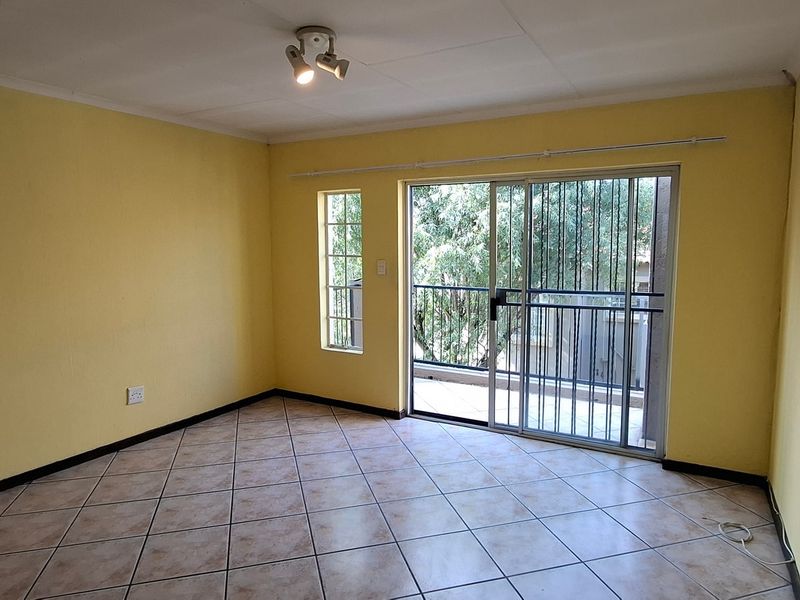 An empty living room featuring tiled flooring, a sliding glass door with security gate, and access to an outdoor balcony area.