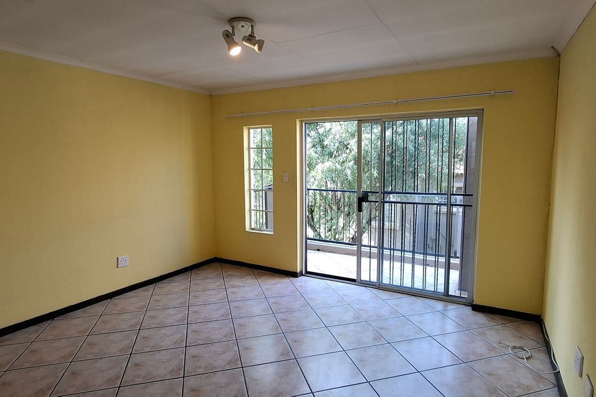 An empty living room featuring tiled flooring, a sliding glass door with security gate, and access to an outdoor balcony area.