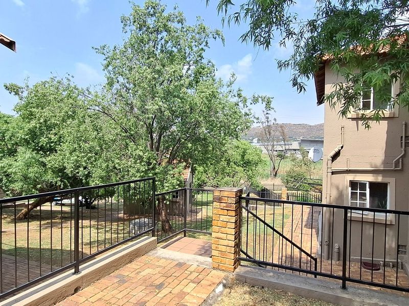Rear exterior view of the apartment complex featuring brick paved patio area, metal balustrades, and established garden surroundings.