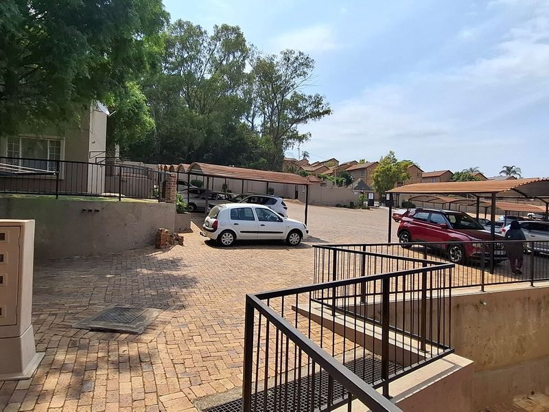 Exterior view of the apartment complex entrance featuring a paved driveway, covered parking carports, and secure metal railings.