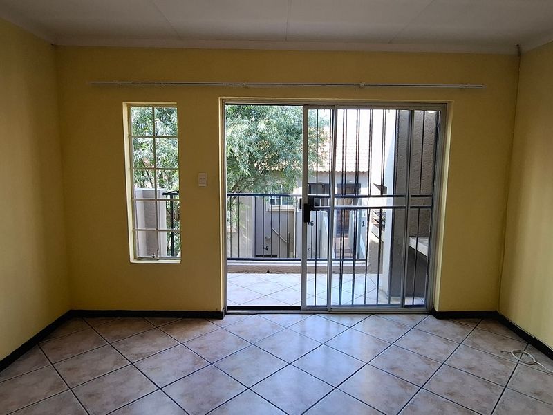 An empty living room featuring tiled flooring, a sliding glass door with security gate, and access to an outdoor balcony area.