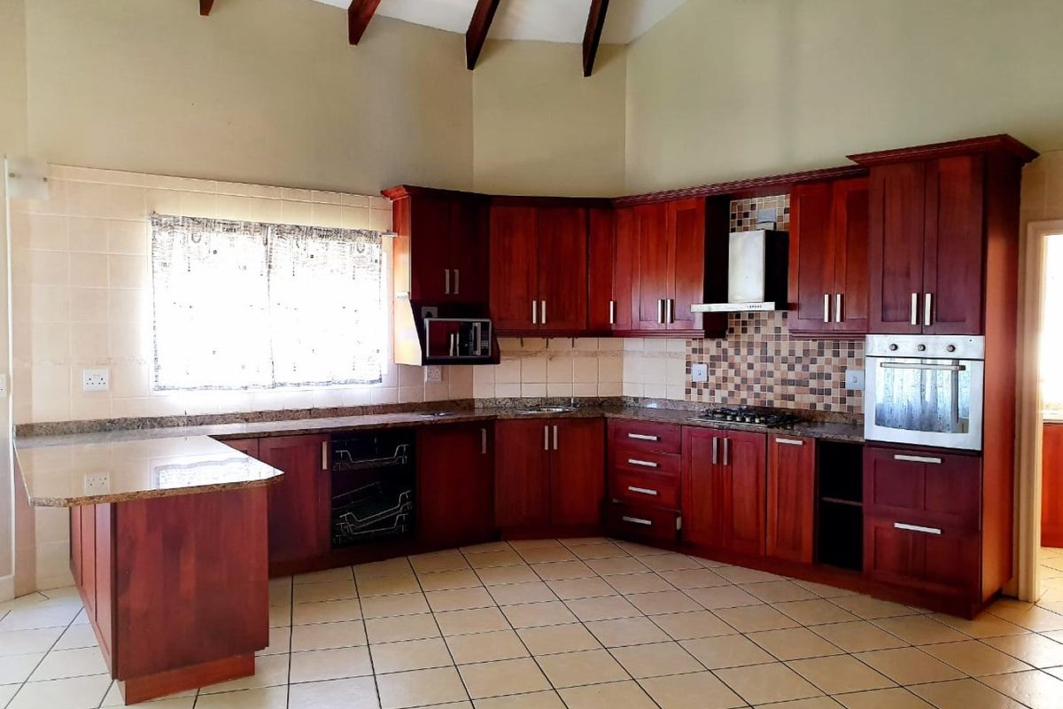 Spacious kitchen featuring rich wooden cabinetry, granite countertops, built-in oven, gas hob, and a high vaulted ceiling with exposed timber beams.