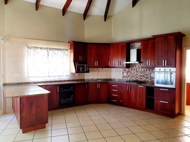 Spacious kitchen featuring rich wooden cabinetry, granite countertops, built-in oven, gas hob, and a high vaulted ceiling with exposed timber beams.