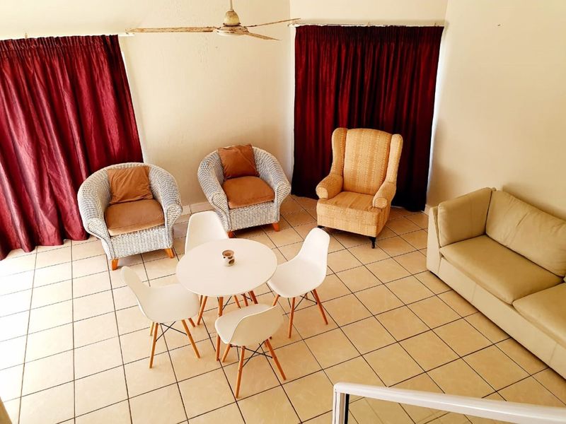 A living area featuring ceramic floor tiles and a ceiling fan, with large windows covered by dark red curtains.