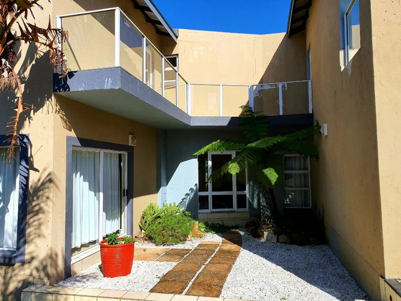 Rear courtyard area featuring a paved walkway, gravel landscaping, and an upper-level balcony with a modern glass balustrade.