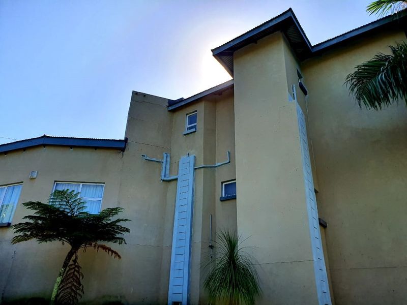 Rear elevation of the property featuring plastered walls, corrugated metal roofing, and visible external plumbing infrastructure.
