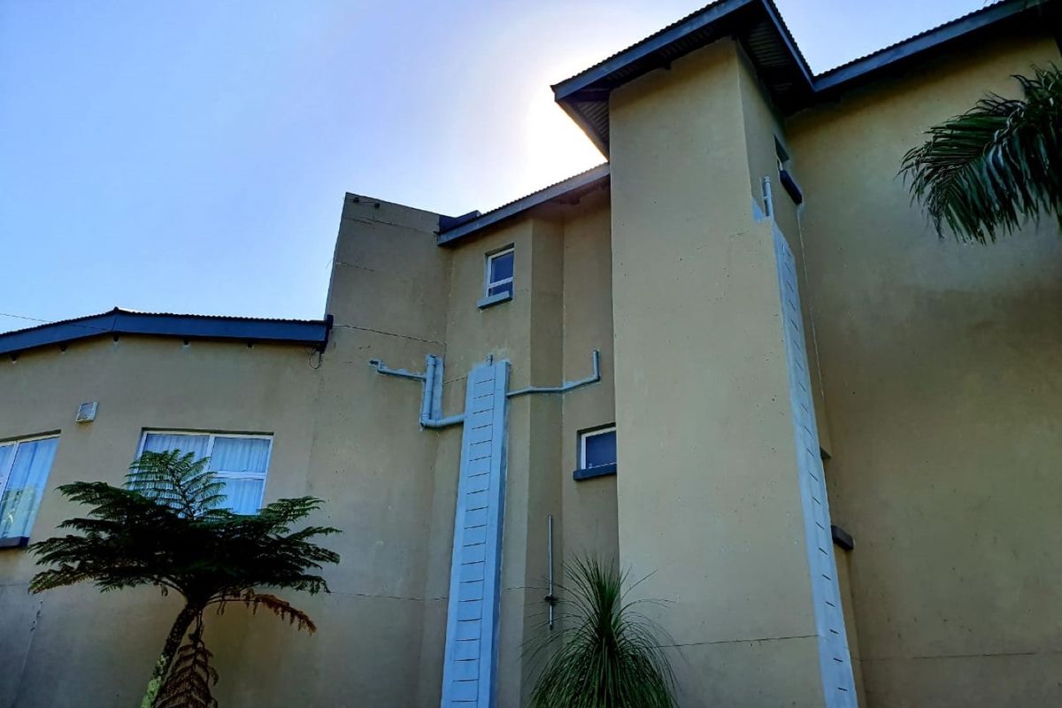 Rear elevation of the property featuring plastered walls, corrugated metal roofing, and visible external plumbing infrastructure.