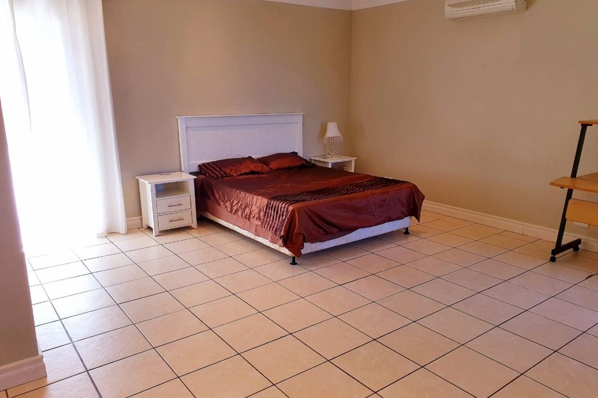 Spacious bedroom featuring neutral tiled flooring, crown molding, and a wall-mounted split-system air conditioner with access to an outdoor area via sliding glass doors.