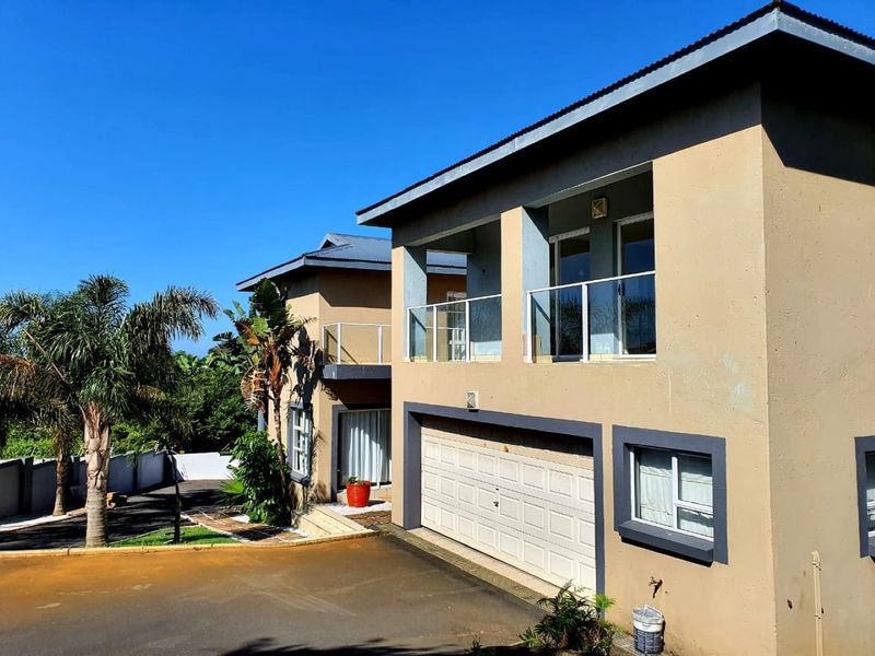 A two-story residential exterior featuring a double garage, upper-level balcony with glass balustrades, and a paved driveway.