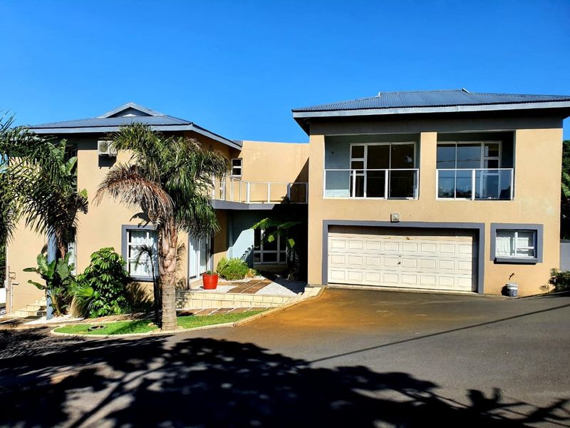 A modern double-story residential property featuring a double garage, upper-level balcony with glass balustrades, and a paved driveway.