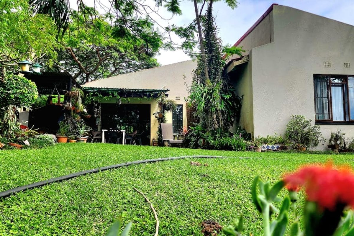 A view of the rear garden and patio area, featuring a well-maintained lawn and established greenery against the house exterior.
