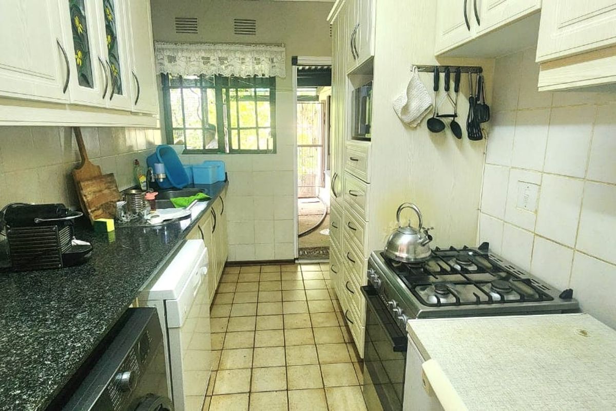 A functional galley-style kitchen featuring granite countertops, a gas hob, built-in oven, and ample cabinetry, with direct access to an outdoor area.