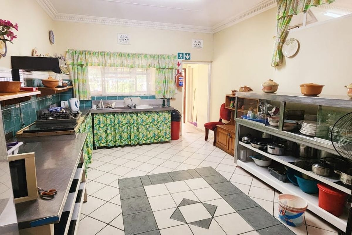 A functional kitchen featuring stainless steel countertops, a gas hob, double basin sink, and tiled flooring with traditional cabinetry.
