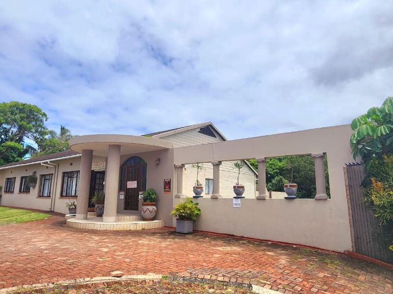 Front exterior view of a commercial property featuring a brick paved driveway, covered entrance porch with decorative columns, and a perimeter boundary wall.