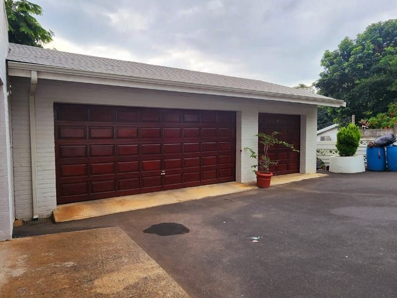 A double and single garage featuring dark wood-finish doors, set against a white brick exterior with an asphalt driveway.