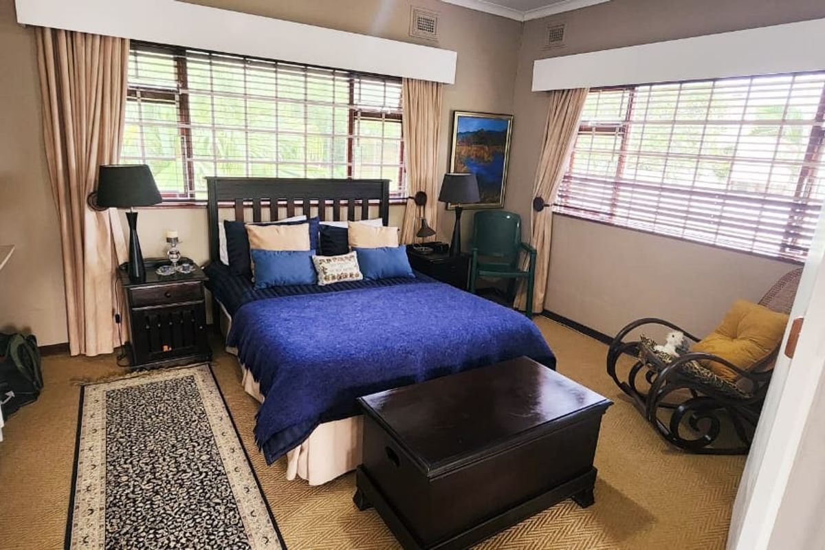 A spacious bedroom featuring large windows, neutral wall tones, carpet flooring, and a built-in wardrobe for storage.