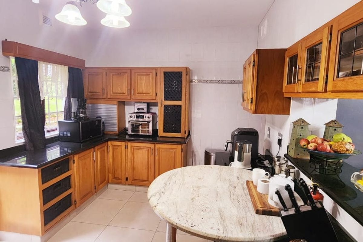 A functional kitchen featuring warm wooden cabinetry, contrasting granite countertops, tiled backsplash, and a built-in breakfast nook with direct access to the garden.