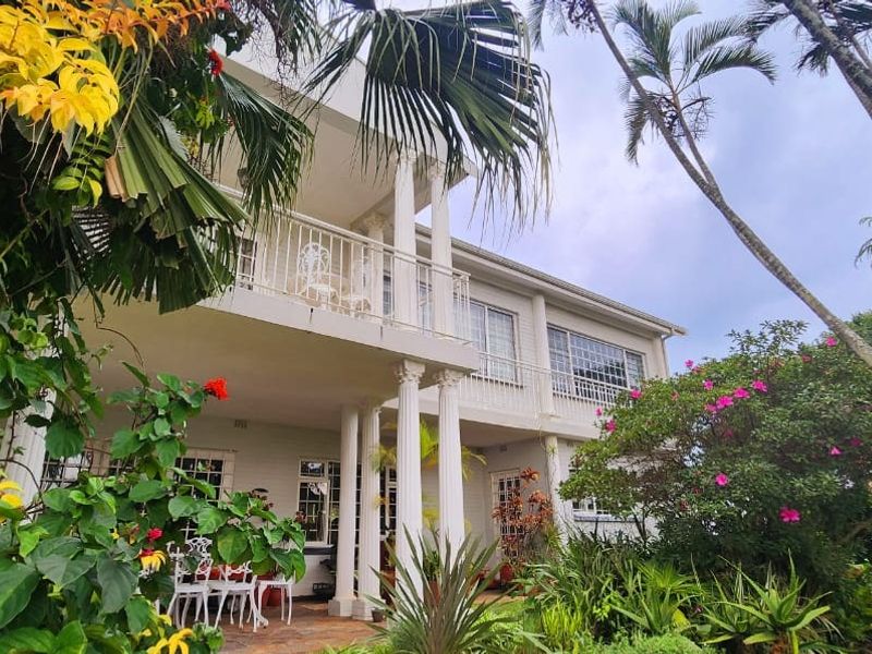 Rear elevation of a two-story house featuring a covered ground-floor patio, an upper-level balcony with railings, and established garden landscaping.