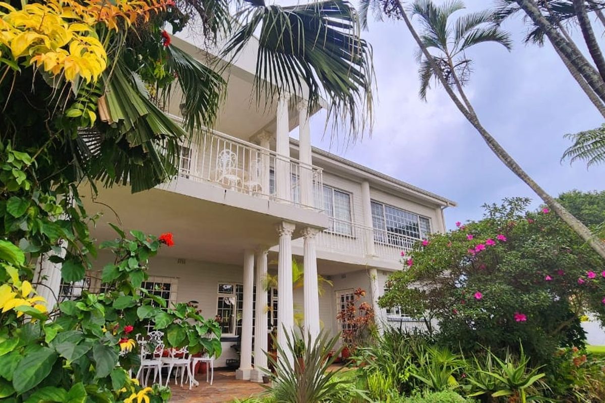 Rear elevation of a two-story house featuring a covered ground-floor patio, an upper-level balcony with railings, and established garden landscaping.