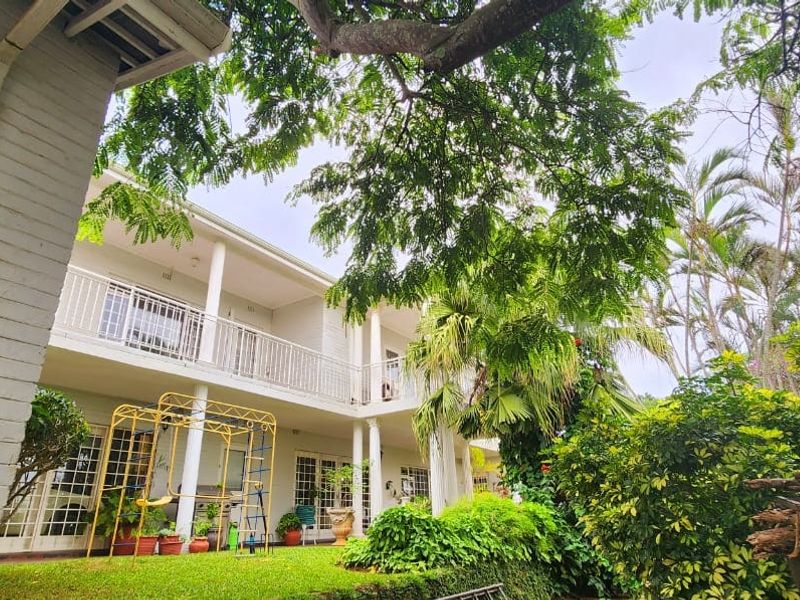 Rear view of a two-story house featuring a balcony with metal railings, support columns, and a landscaped garden area.