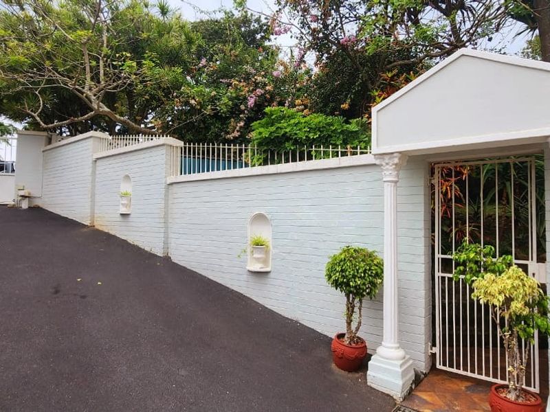 Front entrance area featuring a paved driveway, secure gated access, and a well-maintained brick boundary wall with decorative architectural detailing.
