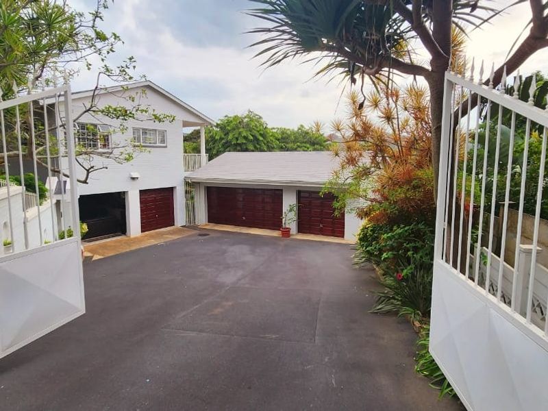 Front view of the property featuring a paved driveway, double garage, and secure gated entrance with established garden surroundings.