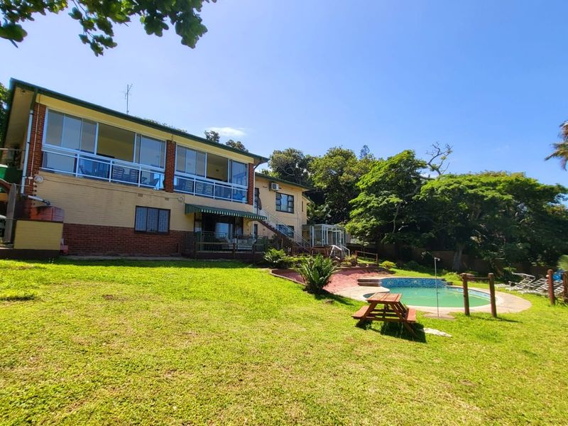 Rear view of the property featuring a spacious lawn, swimming pool, and an elevated balcony with large glass sliding doors.