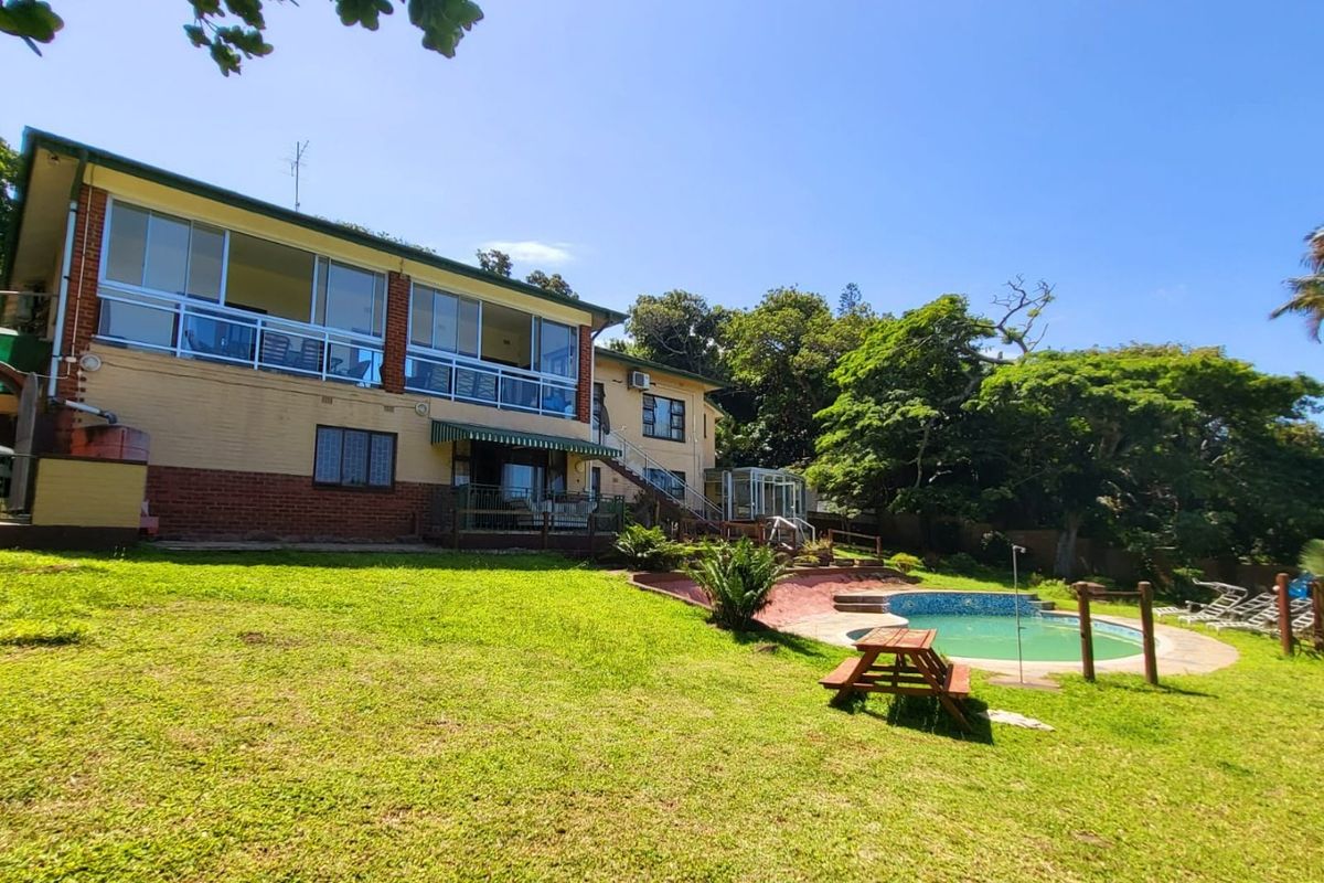 Rear view of the property featuring a spacious lawn, swimming pool, and an elevated balcony with large glass sliding doors.