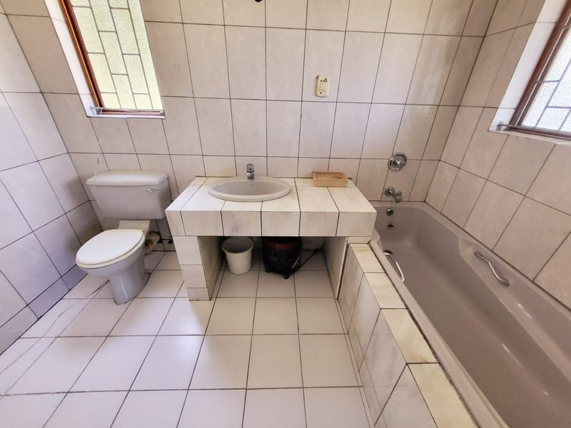 A dated bathroom featuring a tiled vanity with inset basin, a built-in bathtub, and full-height ceramic wall tiling.