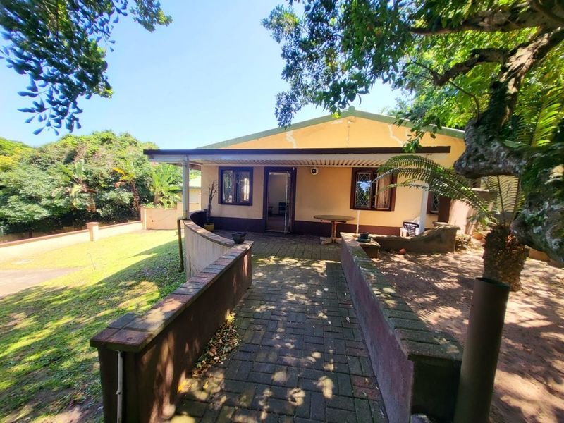 Rear exterior view of the house featuring a paved walkway, covered patio area, and established garden surroundings.