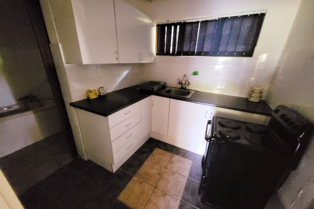 A compact kitchen featuring white cabinetry, dark laminate countertops, a stainless steel sink, and tiled flooring.