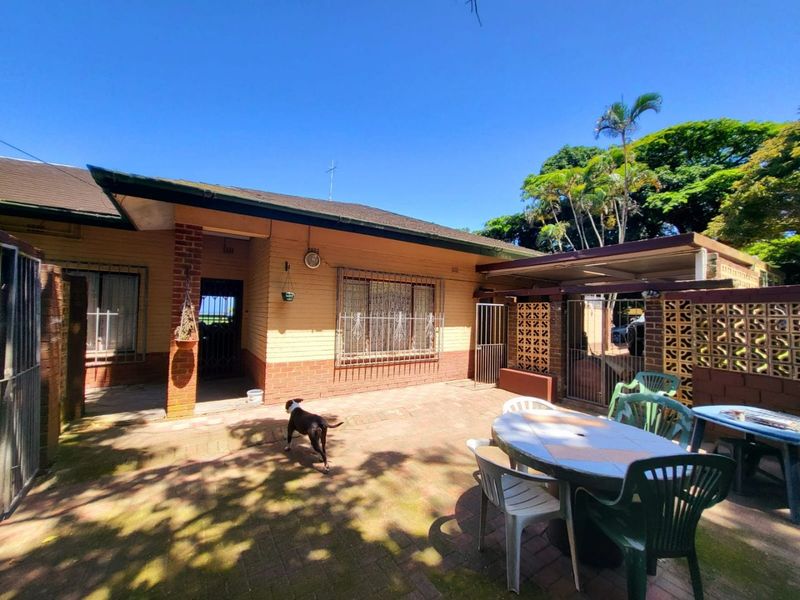 Rear exterior view of the house featuring a paved patio area, brick facade, and security features on windows.