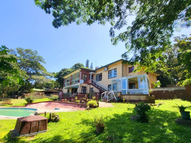 Rear view of a multi-level house featuring a swimming pool, enclosed patio, balcony, and external staircase set within a spacious garden.