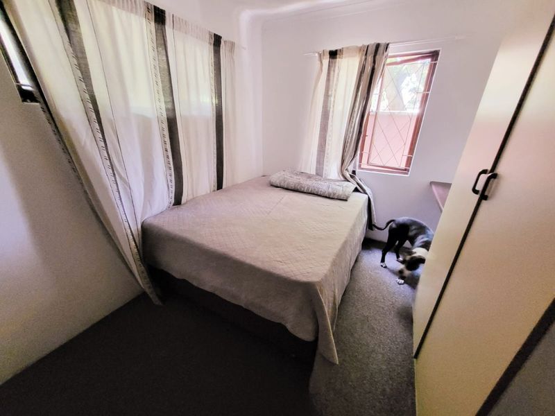 A compact bedroom featuring a built-in wardrobe and security bars on the window, providing a functional and secure sleeping space.
