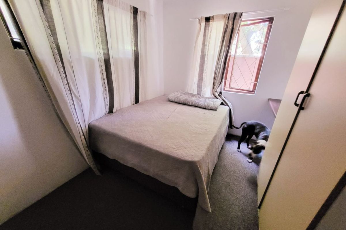 A compact bedroom featuring a built-in wardrobe and security bars on the window, providing a functional and secure sleeping space.