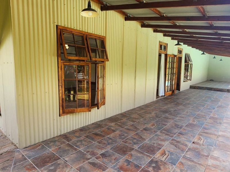 A spacious covered patio featuring tiled flooring, exposed timber rafters, and corrugated metal exterior walls, providing direct access to the garden and pool area.