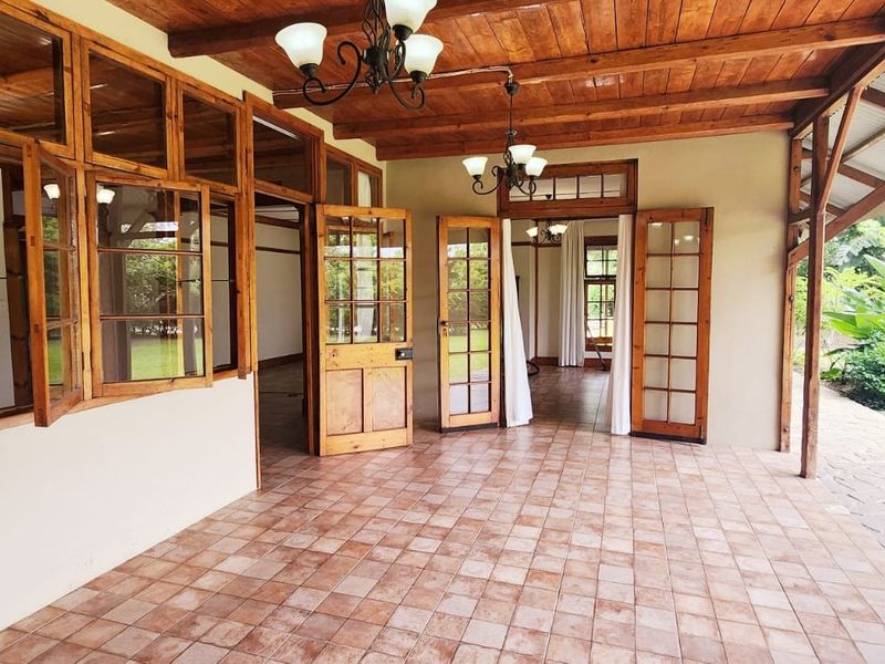 A spacious covered patio featuring tiled flooring, exposed timber ceiling beams, and multiple timber-framed doors providing access to the interior living spaces.