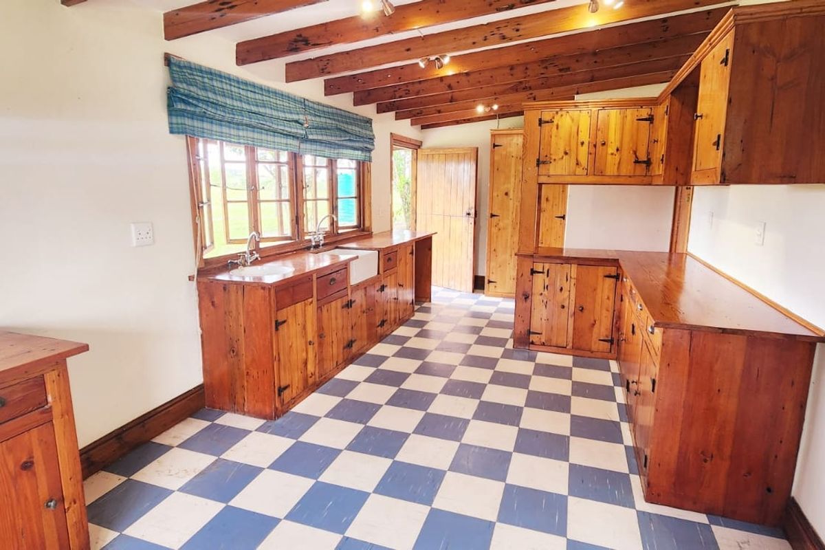 A rustic farmhouse kitchen featuring exposed timber ceiling beams, traditional wooden cabinetry, a farmhouse sink, and distinctive blue and white checkered floor tiles.