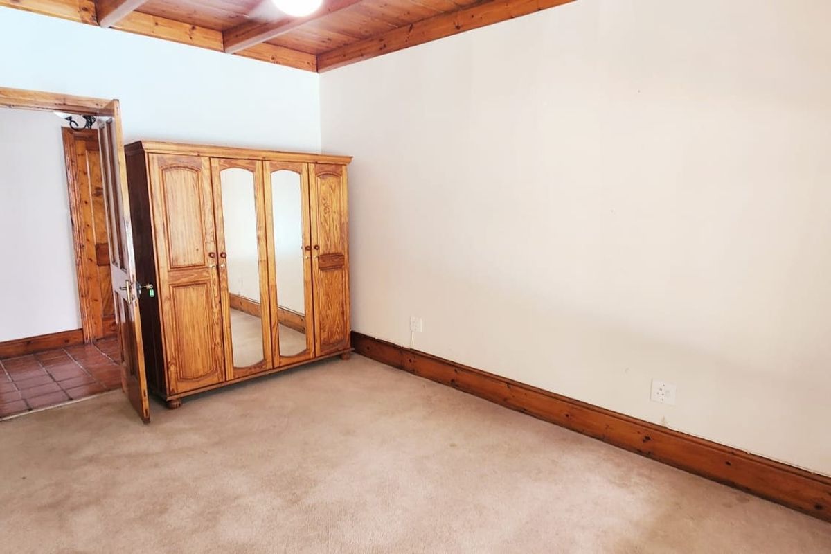A bedroom featuring exposed timber ceiling beams, timber skirting boards, and carpeted flooring, providing a rustic aesthetic.