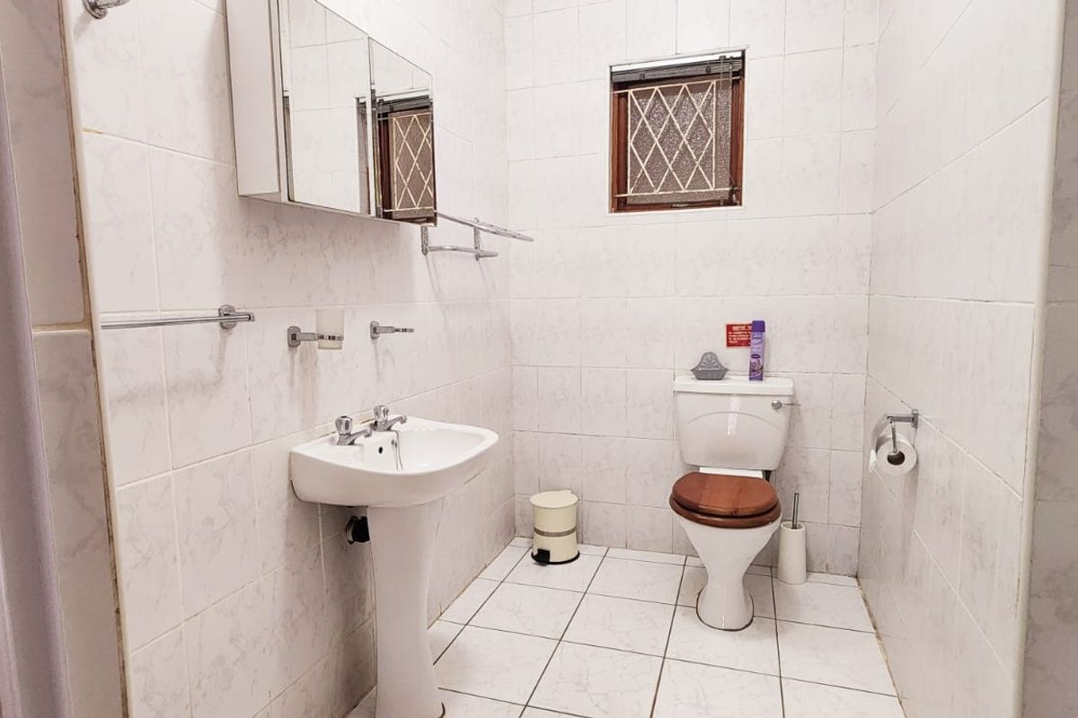 A functional bathroom featuring a pedestal basin, toilet, medicine cabinet, and fully tiled walls and flooring.