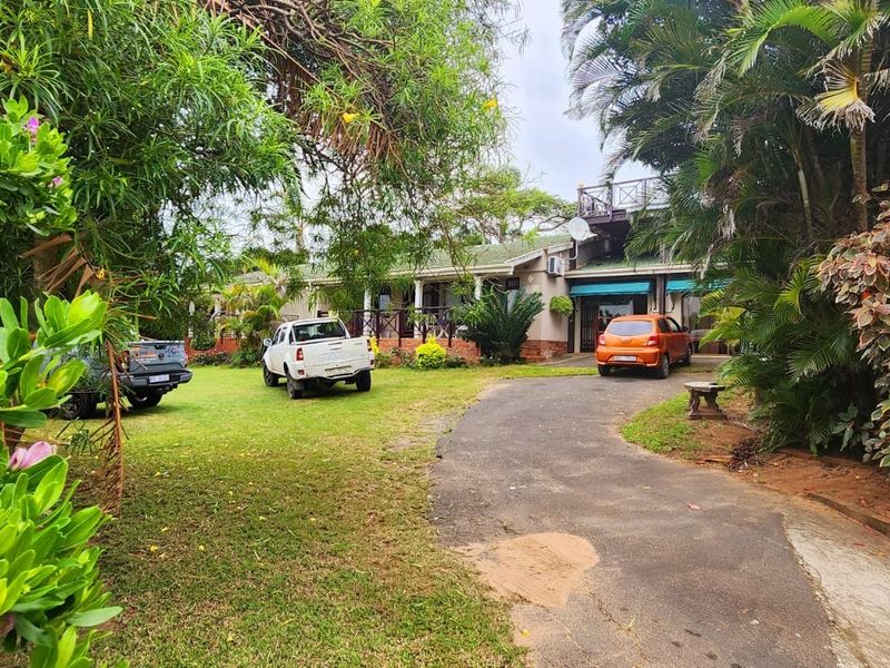 Front view of the property featuring a paved driveway, established garden, and a covered veranda with timber balustrades.