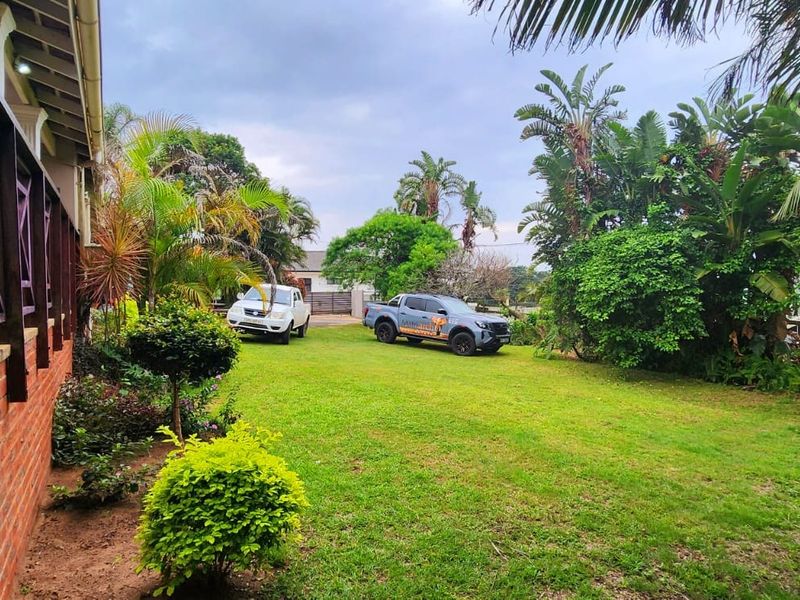 A view of the rear garden and lawn area, featuring a brick-walled house with a timber veranda railing.
