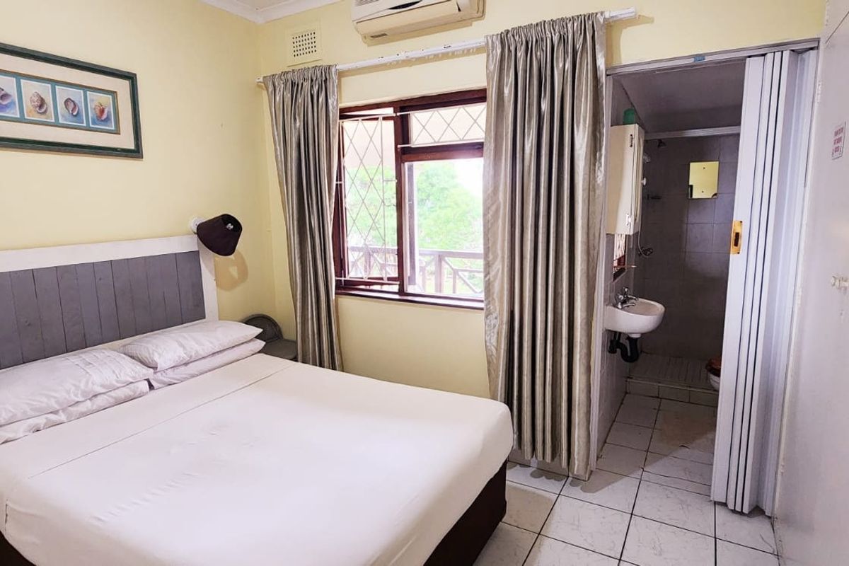 A bedroom featuring an en-suite bathroom, tiled flooring, and an integrated air conditioning unit, requiring cosmetic updates to improve its overall appeal.