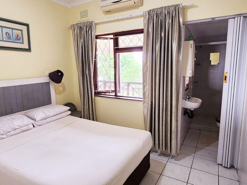 A bedroom featuring an en-suite bathroom, tiled flooring, and an integrated air conditioning unit, requiring cosmetic updates to improve its overall appeal.