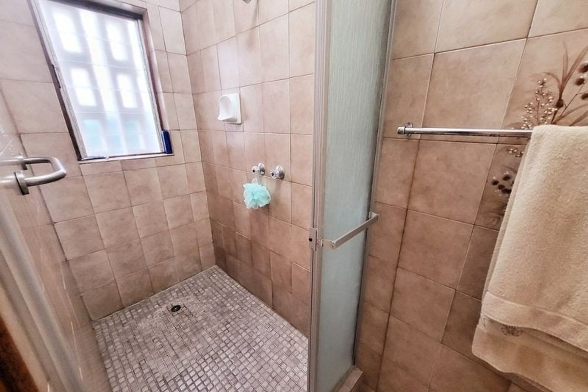 A functional bathroom shower area featuring floor-to-ceiling wall tiles, a mosaic tiled shower floor, and a glass shower enclosure.