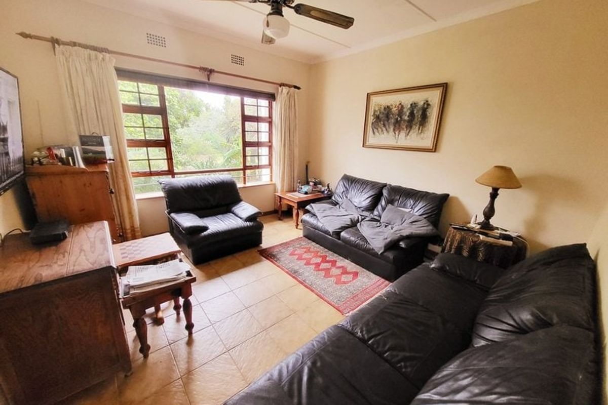 A living room featuring tiled flooring, a ceiling fan, and a large window providing natural light.
