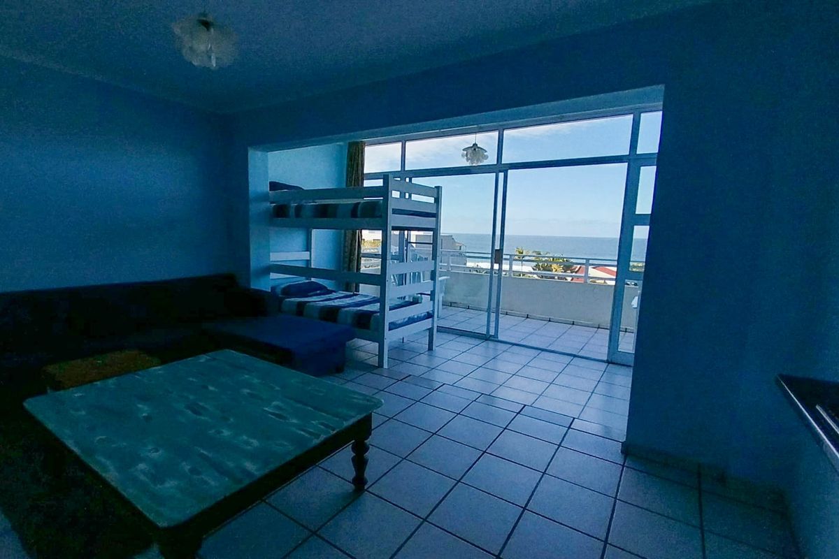 Spacious living area featuring tiled flooring and large sliding glass doors that open onto a balcony with ocean views.