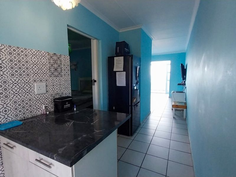 A kitchen area featuring a patterned tile backsplash, stone-look countertop, and built-in cabinetry, leading into an adjacent living space with tiled flooring throughout.